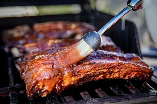 Ribs being cooked on a grill with a spatula.